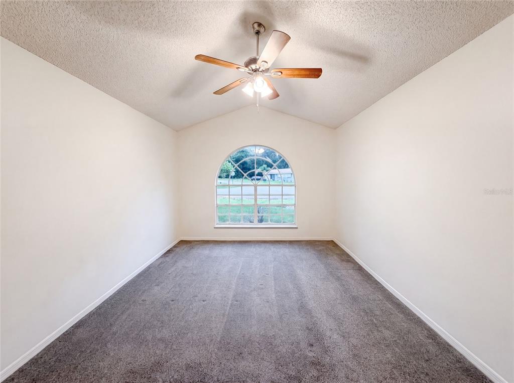 An empty room with beige walls, gray carpet, a vaulted ceiling, and an arched window — 29 VALENCIA CIRCLE, DEBARY, FL