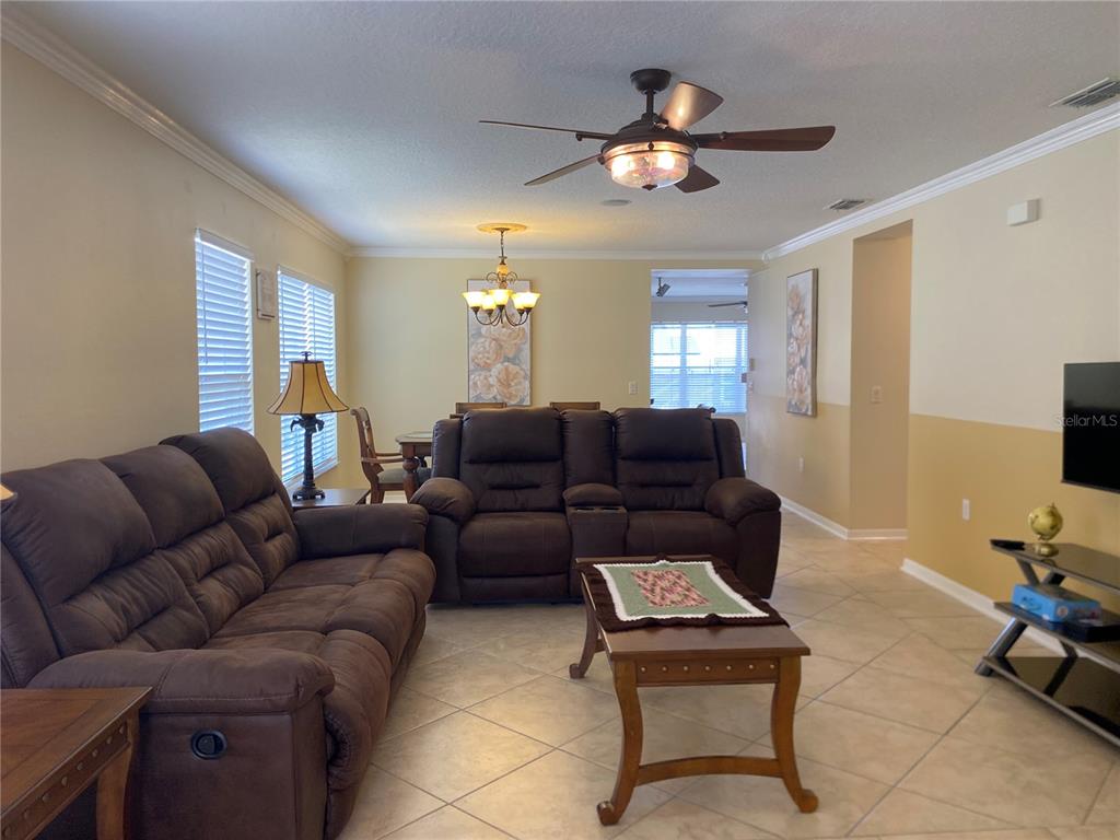 A living room with tile floors, brown reclining sofas, a coffee table, and a dining area — 662 ROSSELLI BOULEVARD, DAVENPORT, FL