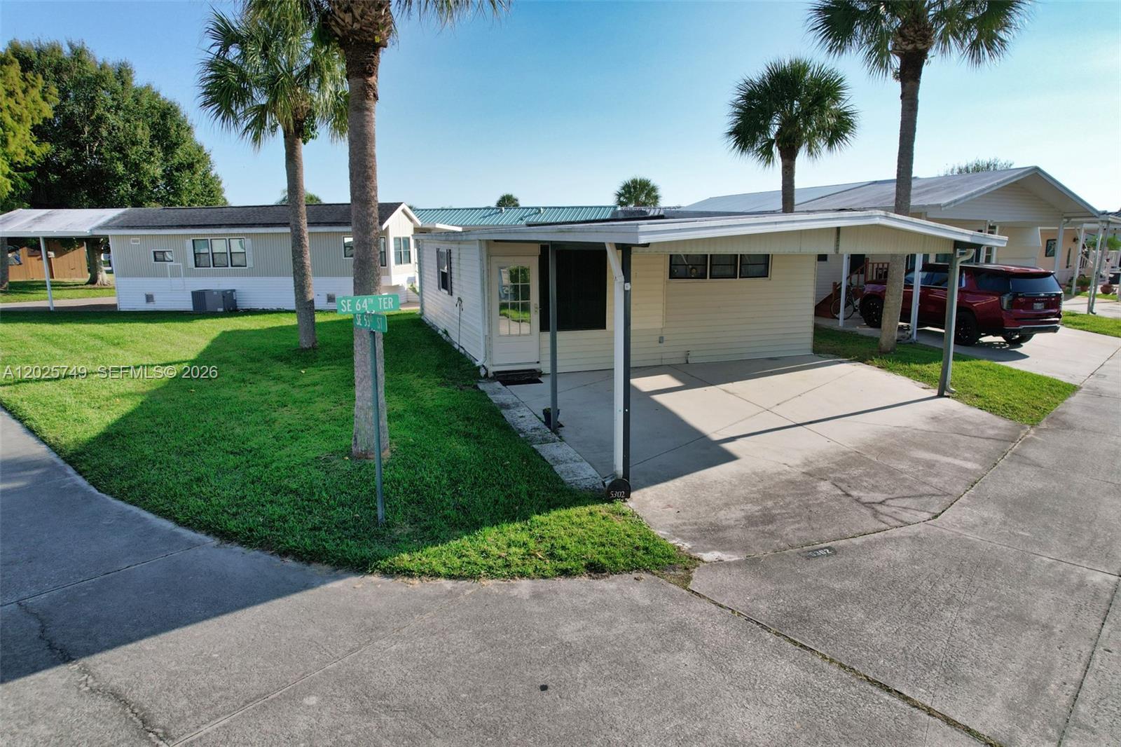 A single-story mobile home features a carport, palm trees, and a grassy corner lot — 5302 SE 64TH TERR, Okeechobee FL 34974, OKEECHOBEE, FL