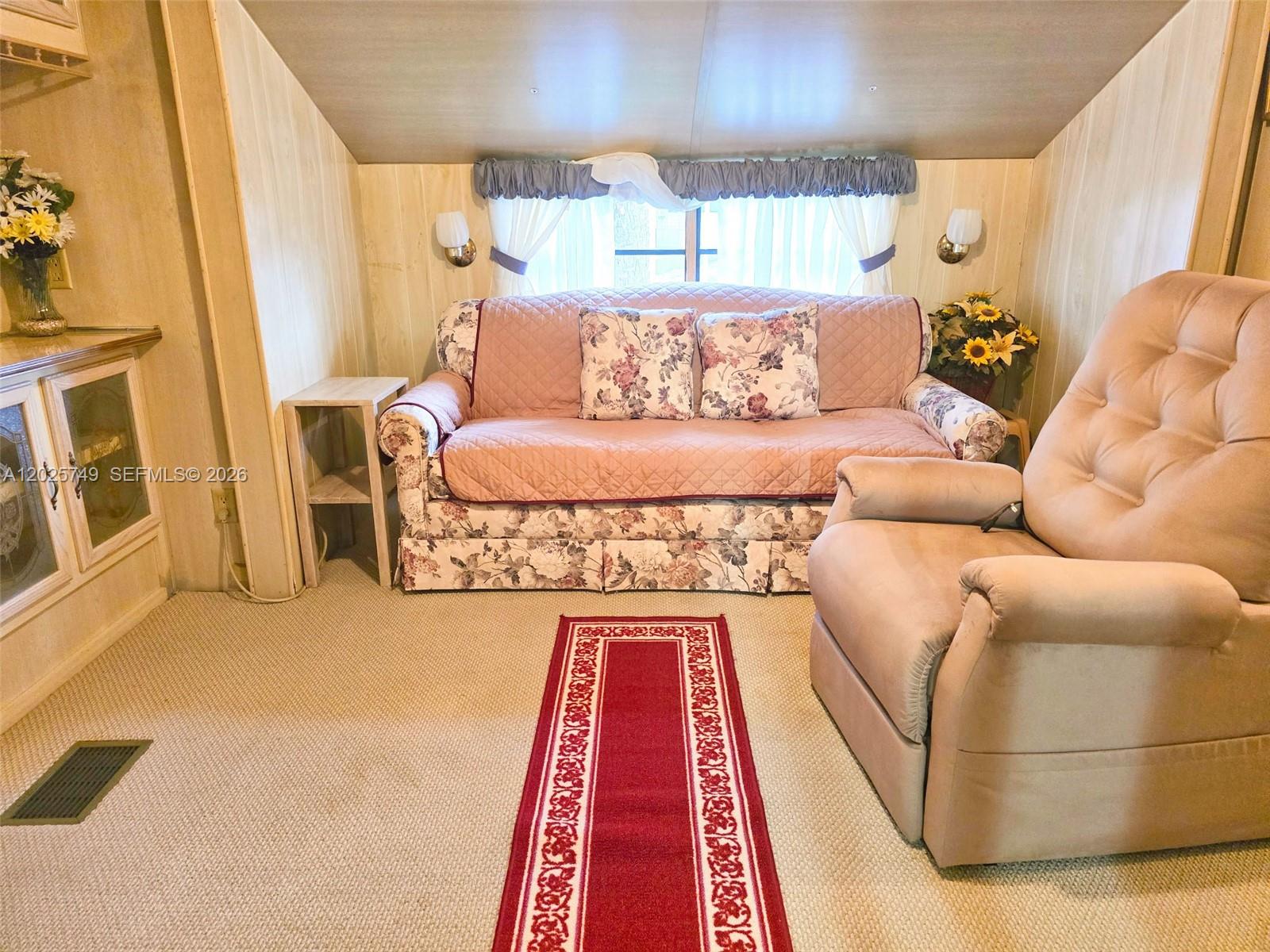 A living room features wood-paneled walls, a floral sofa, a recliner, and a red rug — 5302 SE 64TH TERR, Okeechobee FL 34974, OKEECHOBEE, FL