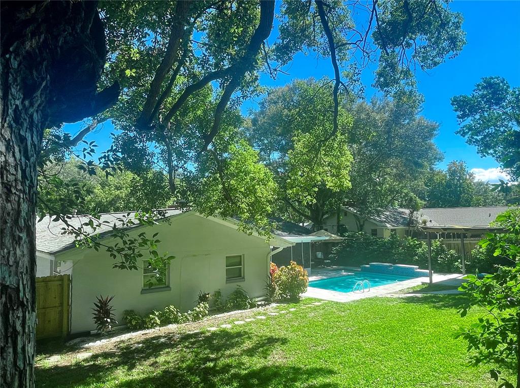 A backyard features a white house, a swimming pool, and mature trees under a blue sky — 764 FOREST GLEN ROAD, CLEARWATER, FL