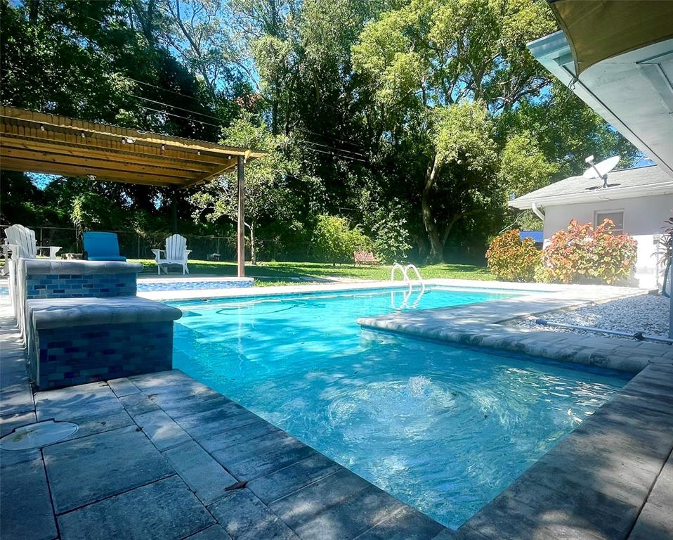 A backyard swimming pool with a stone patio, a wooden pergola, and a house exterior — 764 FOREST GLEN ROAD, CLEARWATER, FL