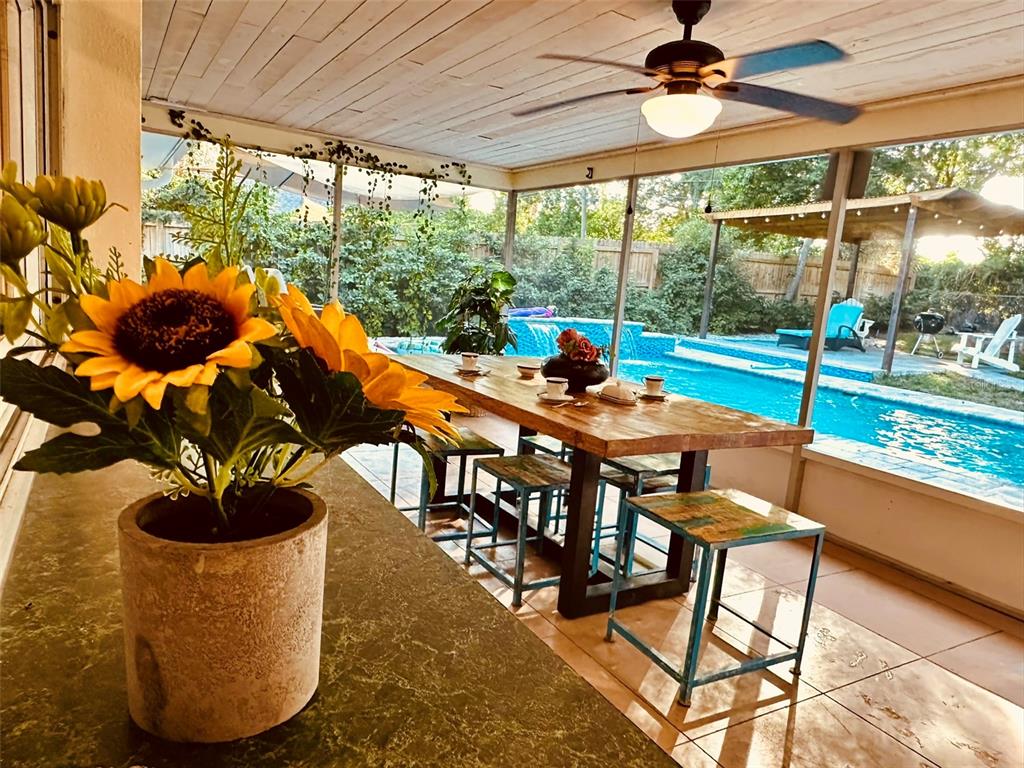 A screened-in patio features a wooden dining table, stools, and a view of a pool — 764 FOREST GLEN ROAD, CLEARWATER, FL