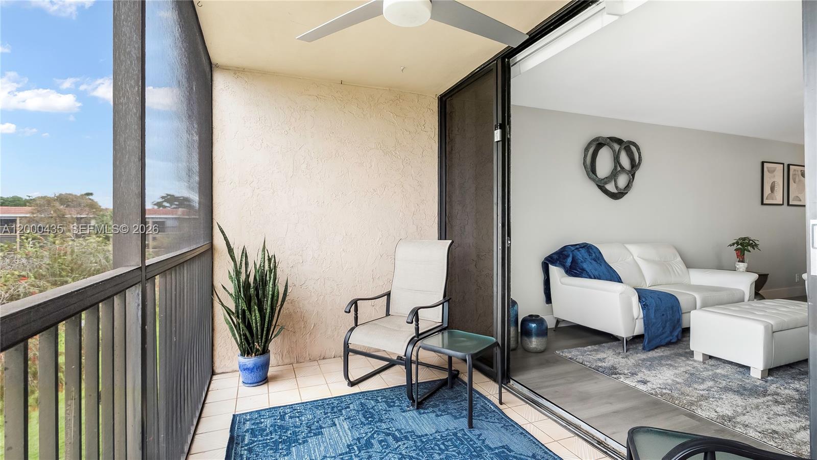 A balcony with a chair and plant overlooks a living room with white furniture — 6231 Coral Lake Dr # 307, Margate FL 33063, MARGATE, FL