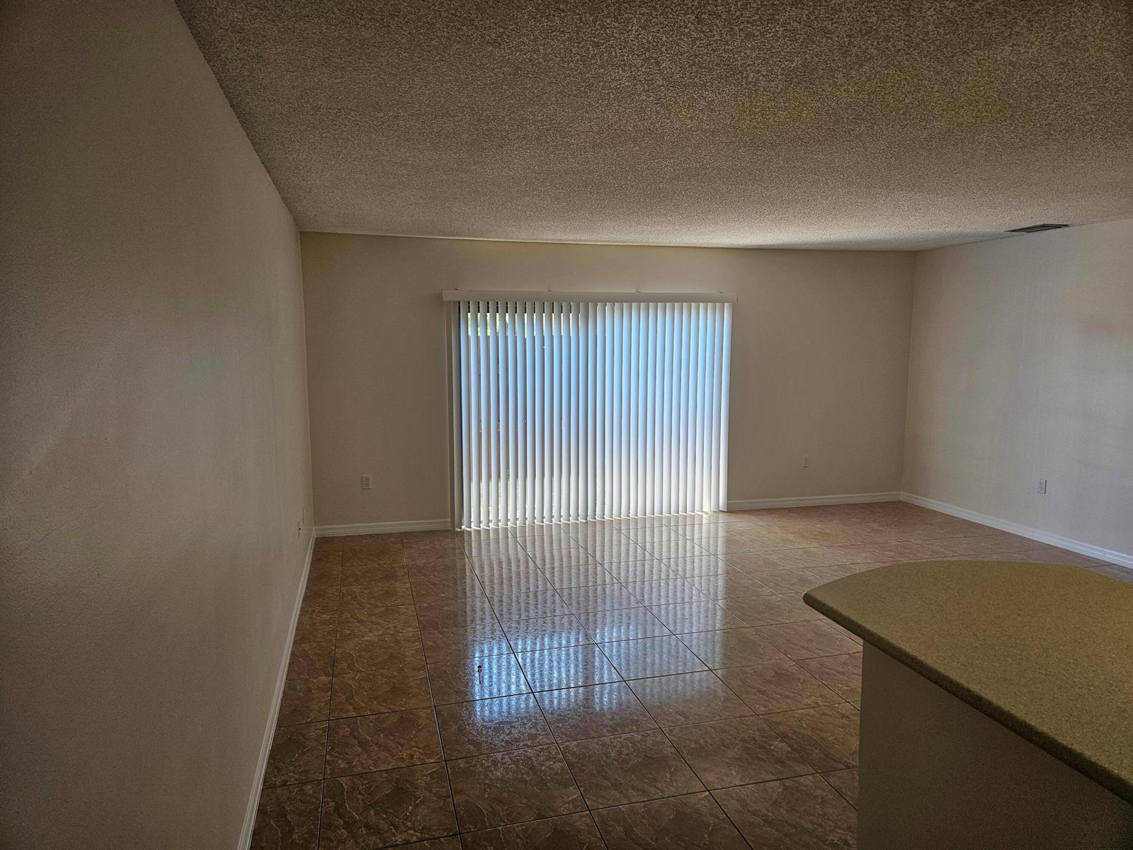An empty room with beige tile flooring, white walls, and vertical blinds over a sliding door — 2050 Oleander Boulevard # 108, Fort Pierce FL 34950, FORT PIERCE, FL