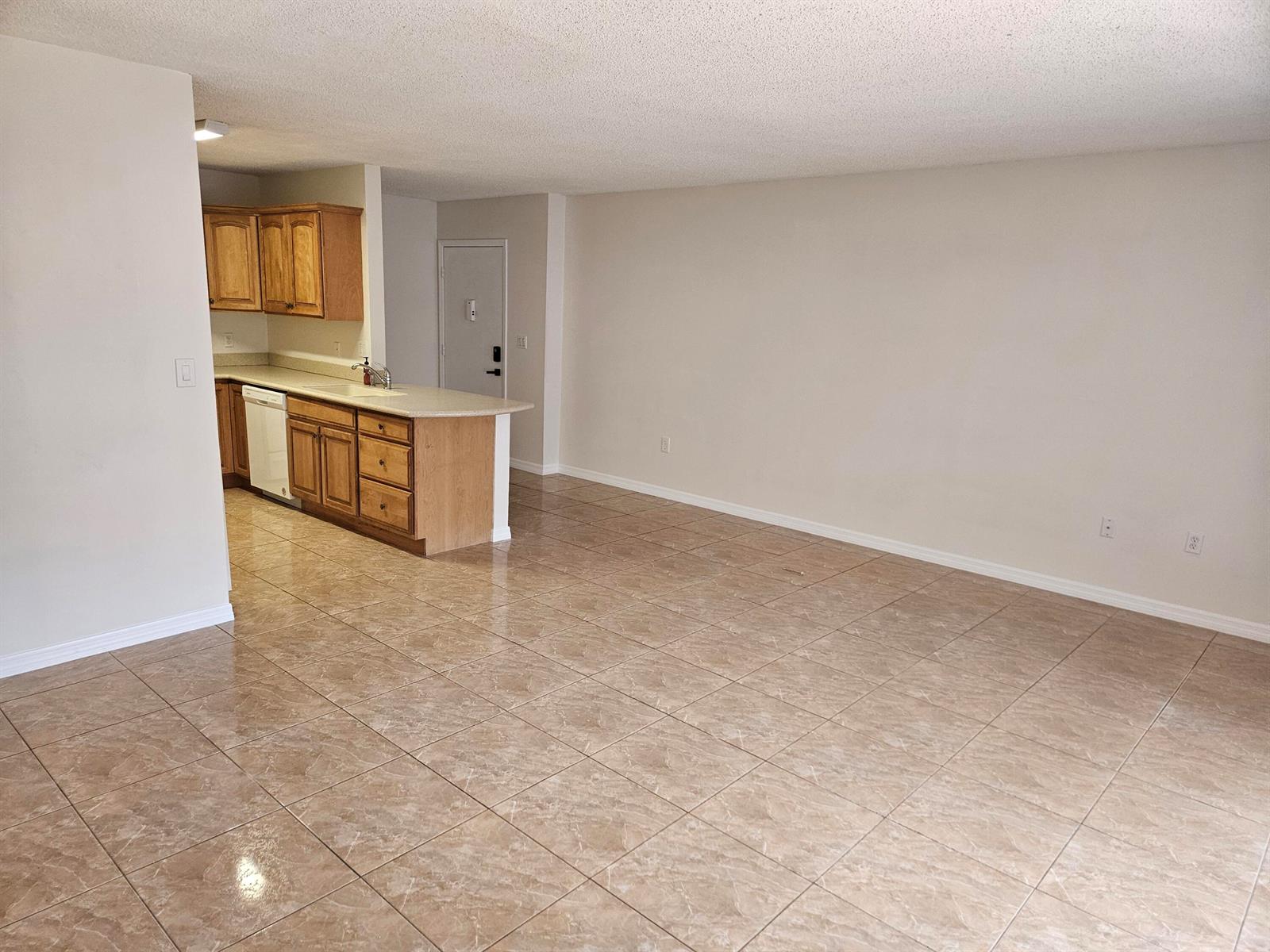 An open-concept living area features light-colored tile flooring, beige walls, and a kitchen with wood cabinets — 2050 Oleander Boulevard # 108, Fort Pierce FL 34950, FORT PIERCE, FL