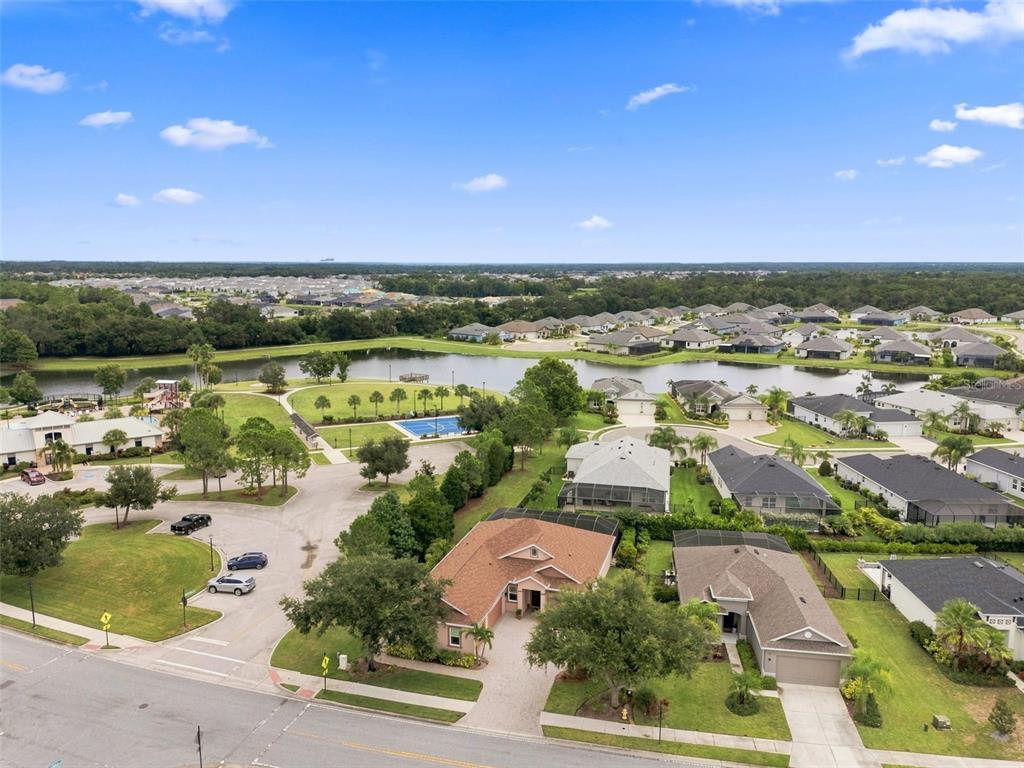 An aerial view shows a suburban neighborhood with houses, a lake, and a sports court — 3850 CREEKSIDE PARK DR, PARRISH, FL