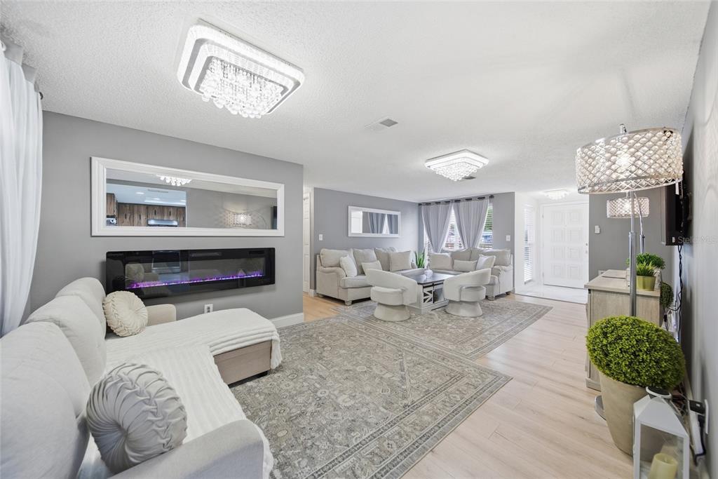 A living room features a fireplace, two chandeliers, light wood flooring, and neutral-toned furniture — 7435 FIRESIDE DRIVE, PORT RICHEY, FL