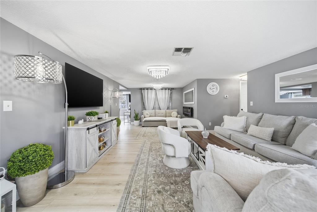 A spacious living room features gray walls, light wood flooring, and two white chandeliers — 7435 FIRESIDE DRIVE, PORT RICHEY, FL