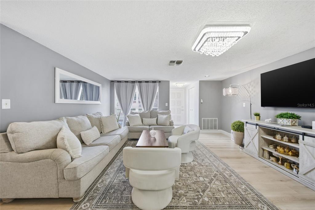 A living room features light gray walls, a large area rug, and a television console — 7435 FIRESIDE DRIVE, PORT RICHEY, FL