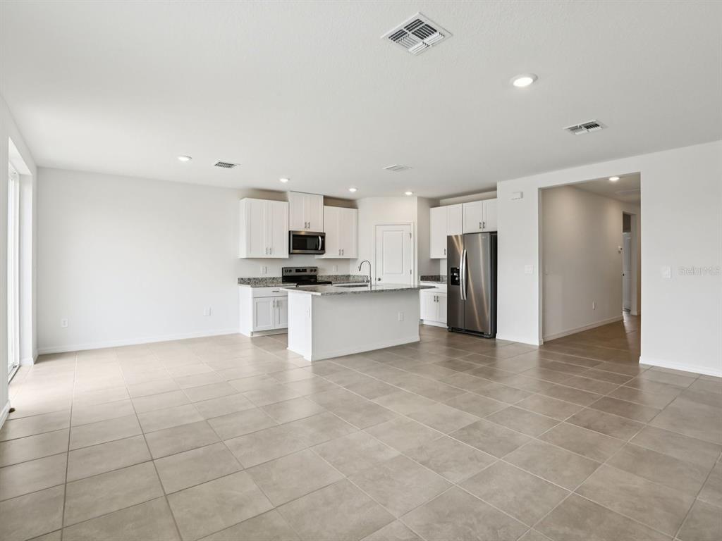 A kitchen with white cabinets, granite countertops, and tile flooring opens into a living area — 1785 FOREST RUN LANE, AUBURNDALE, FL