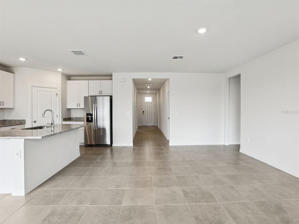 A kitchen with white cabinets and granite countertops overlooks an open living area with tile flooring — 1785 FOREST RUN LANE, AUBURNDALE, FL
