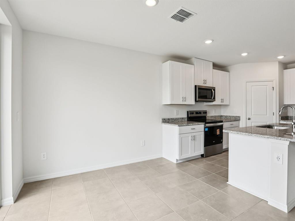 A kitchen features white cabinets, granite countertops, stainless steel appliances, and light-colored tile flooring — 1785 FOREST RUN LANE, AUBURNDALE, FL