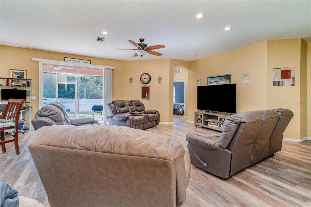 A living room features light wood-look flooring, tan walls, a ceiling fan, and leather furniture — 249 FERDON CIRCLE, PORT CHARLOTTE, FL