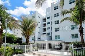 A white multi-story apartment building stands behind a white metal fence and palm trees — 650 GOLDEN GATE POINT UNIT 301, SARASOTA, FL