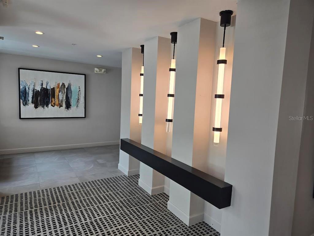 A modern hallway features a black floating shelf, three pendant lights, and abstract wall art — 650 GOLDEN GATE POINT UNIT 301, SARASOTA, FL