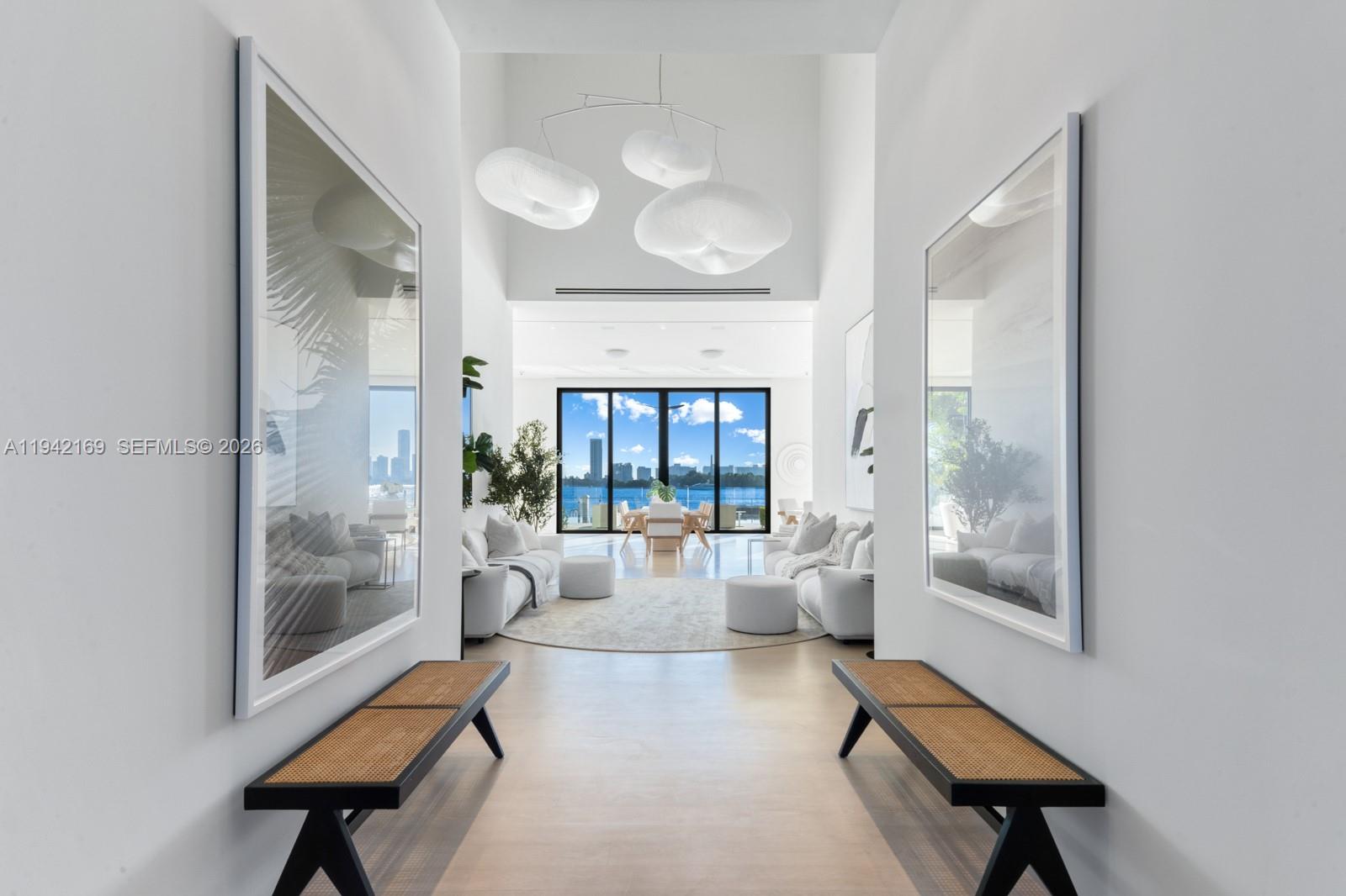 A bright, minimalist hallway leads to a living area with floor-to-ceiling windows and water views — 33 E Dilido Dr, Miami Beach FL 33139, MIAMI BEACH, FL