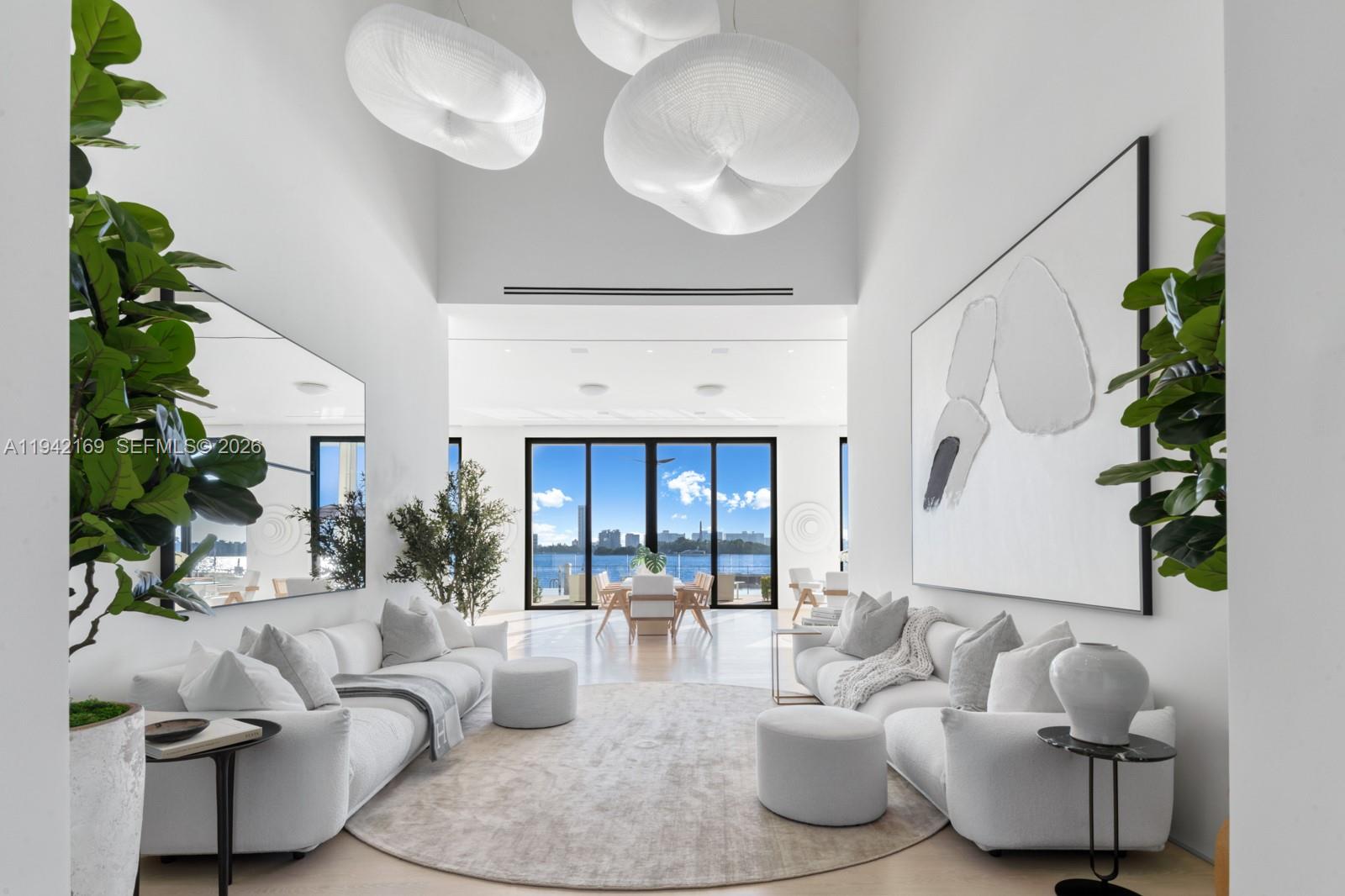 A bright living room features high ceilings, white sofas, large pendant lights, and water views — 33 E Dilido Dr, Miami Beach FL 33139, MIAMI BEACH, FL