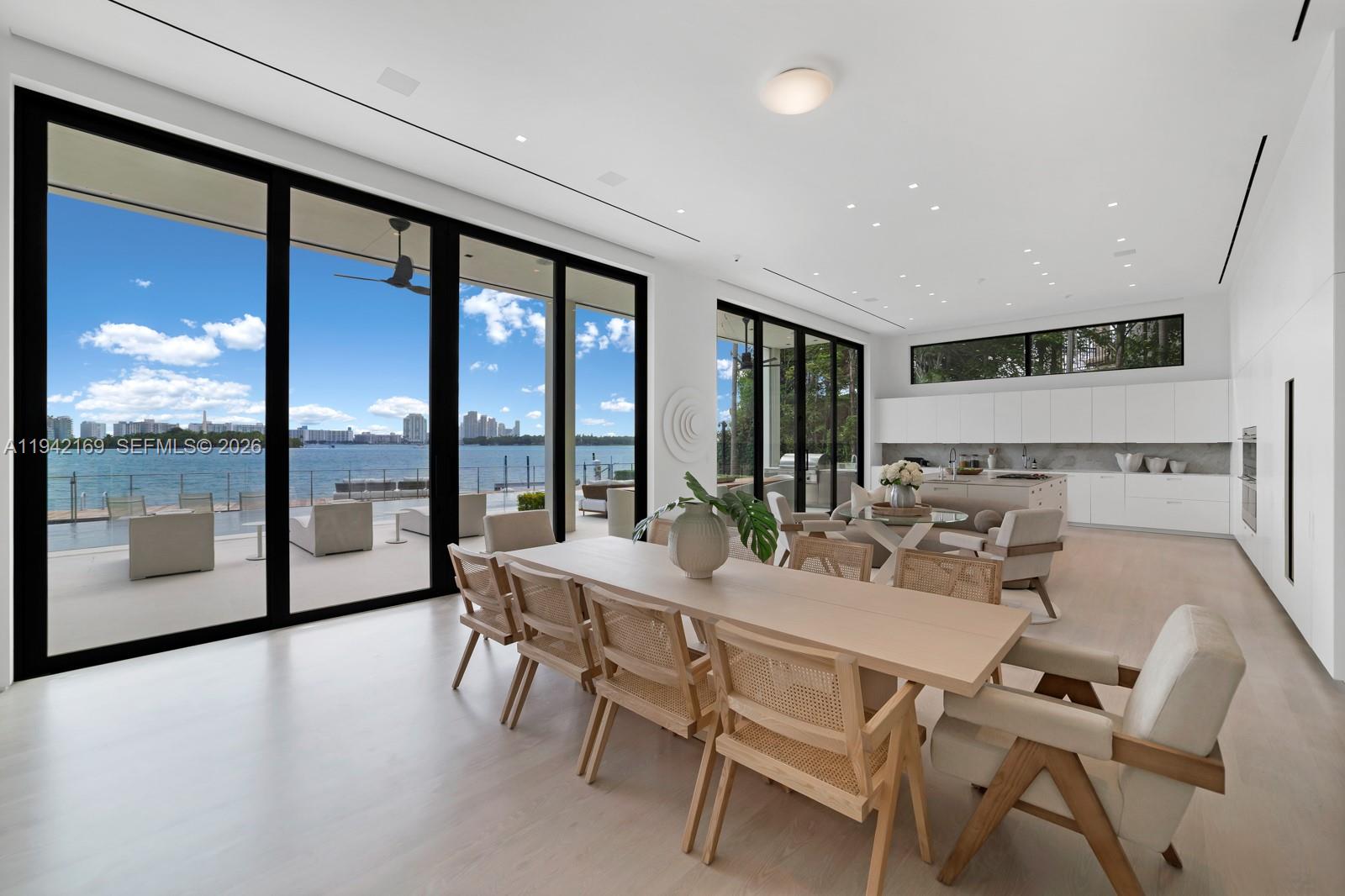 A modern open-plan dining and kitchen area features floor-to-ceiling windows overlooking a waterfront view — 33 E Dilido Dr, Miami Beach FL 33139, MIAMI BEACH, FL