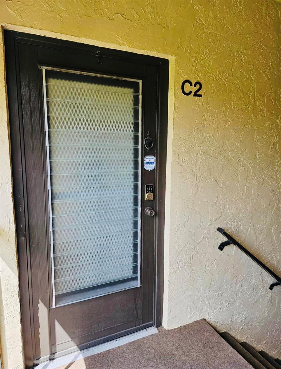 A dark brown front door with a security screen and keypad lock labeled C2 — 443 Pine Glen Lane # 2, FL 33463, FL