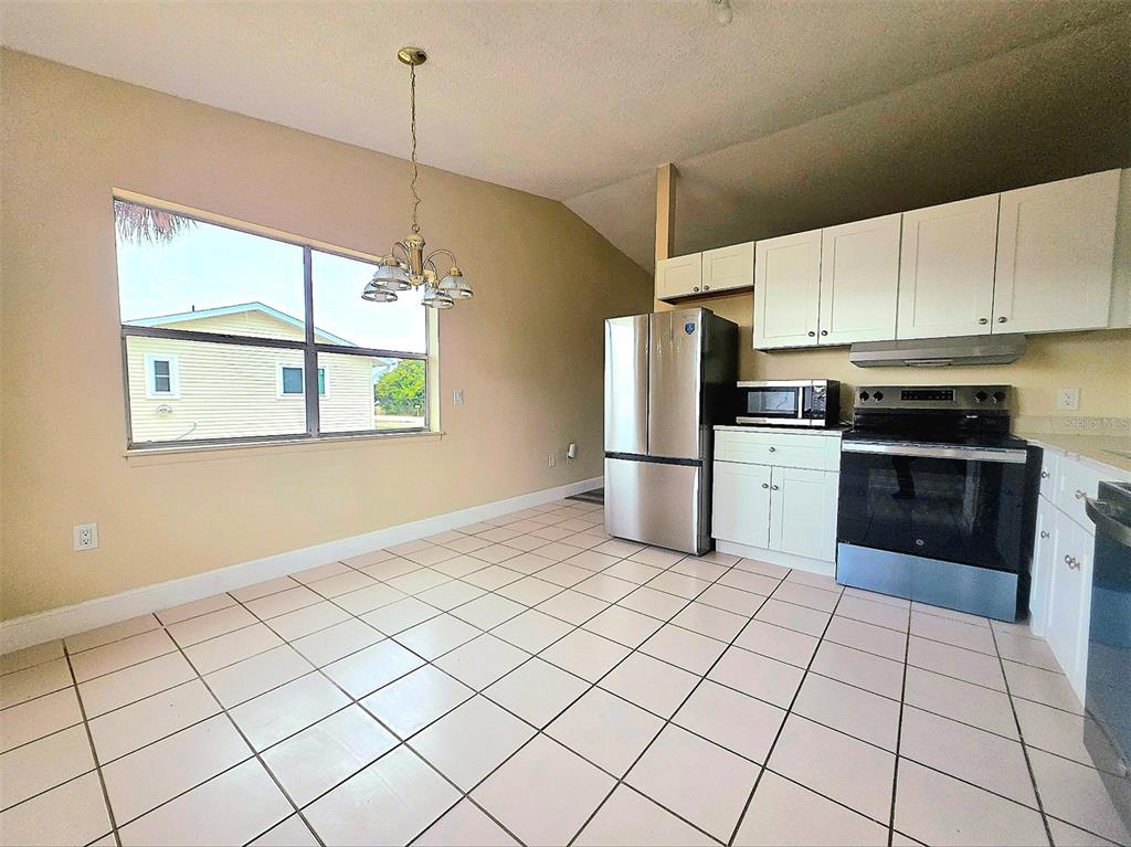 A kitchen and dining area with white cabinets, stainless steel appliances, and tiled flooring — 12091 CROSSGATE AVENUE, PORT CHARLOTTE, FL