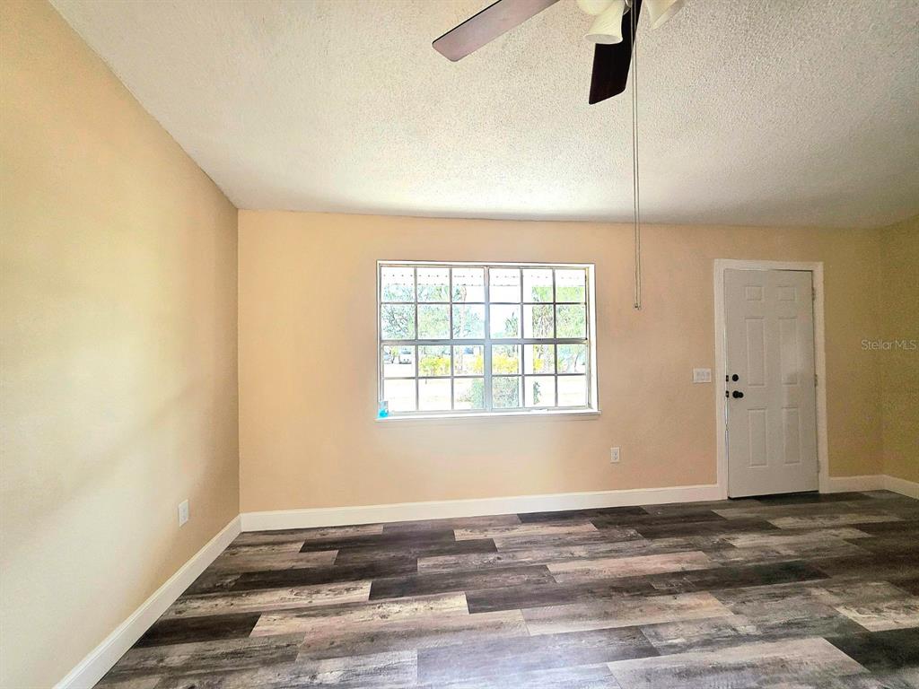 An empty room features light-colored walls, a ceiling fan, and wood-look vinyl plank flooring — 12091 CROSSGATE AVENUE, PORT CHARLOTTE, FL