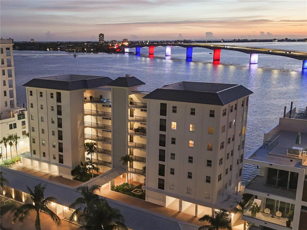 An aerial view shows a multi-story apartment building near a bridge illuminated with red and blue — 226 GOLDEN GATE POINT UNIT 12, SARASOTA, FL
