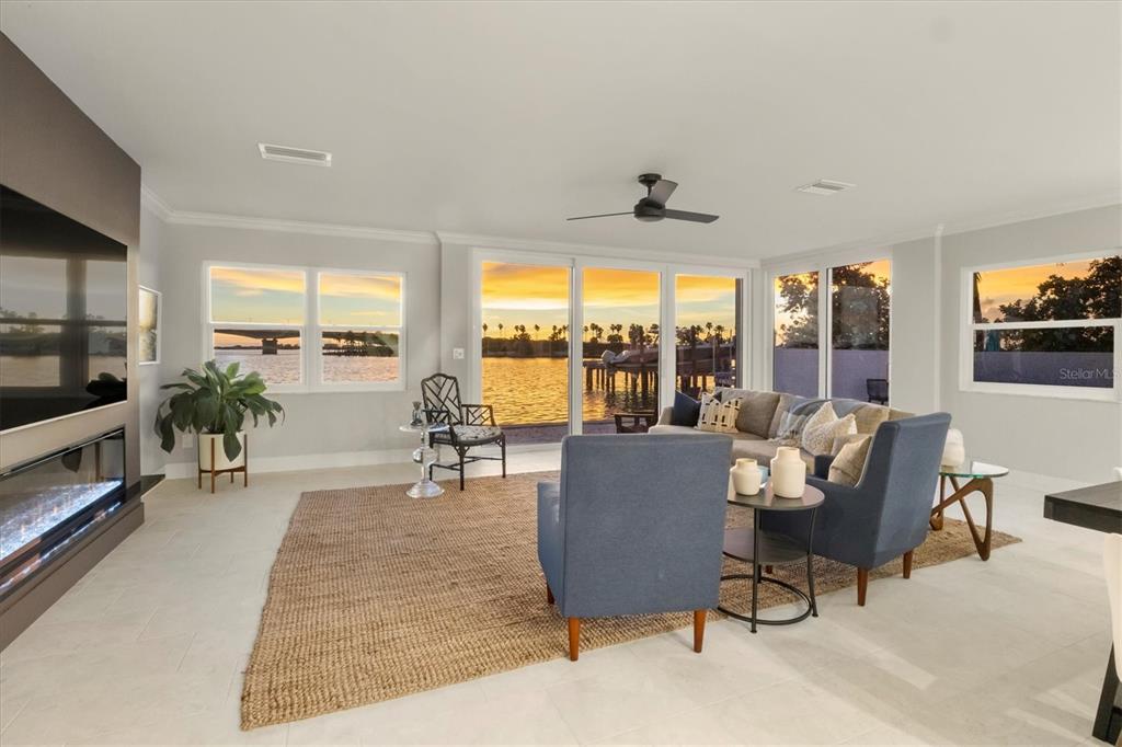 A living room features a fireplace, blue armchairs, a sectional sofa, and floor-to-ceiling waterfront views — 226 GOLDEN GATE POINT UNIT 12, SARASOTA, FL