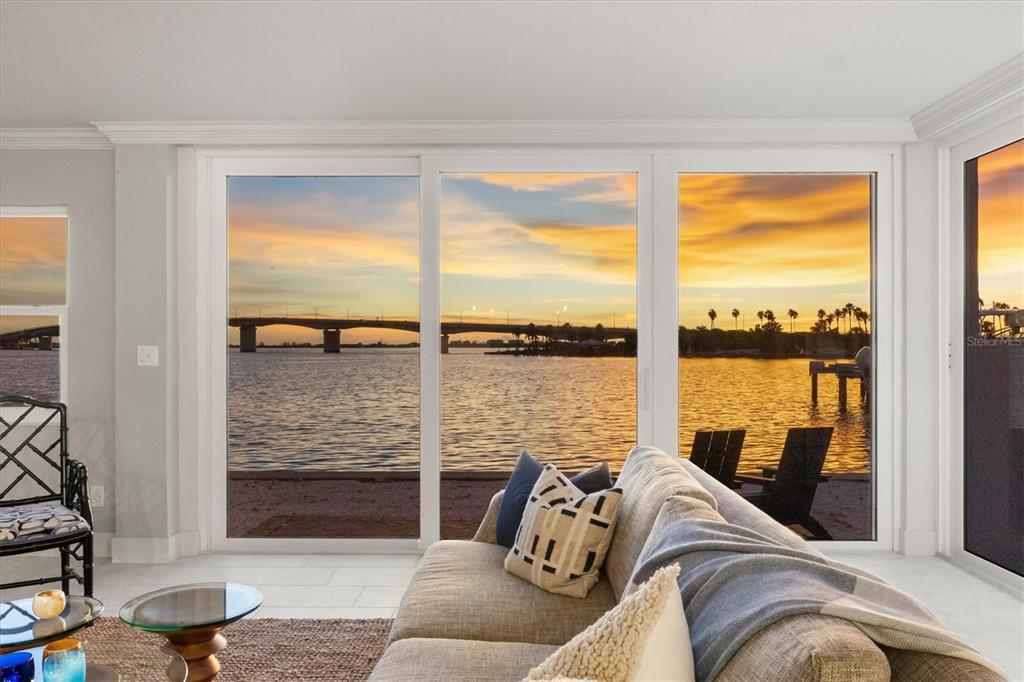 A living room with a sofa faces large sliding glass doors overlooking a sunset water view — 226 GOLDEN GATE POINT UNIT 12, SARASOTA, FL