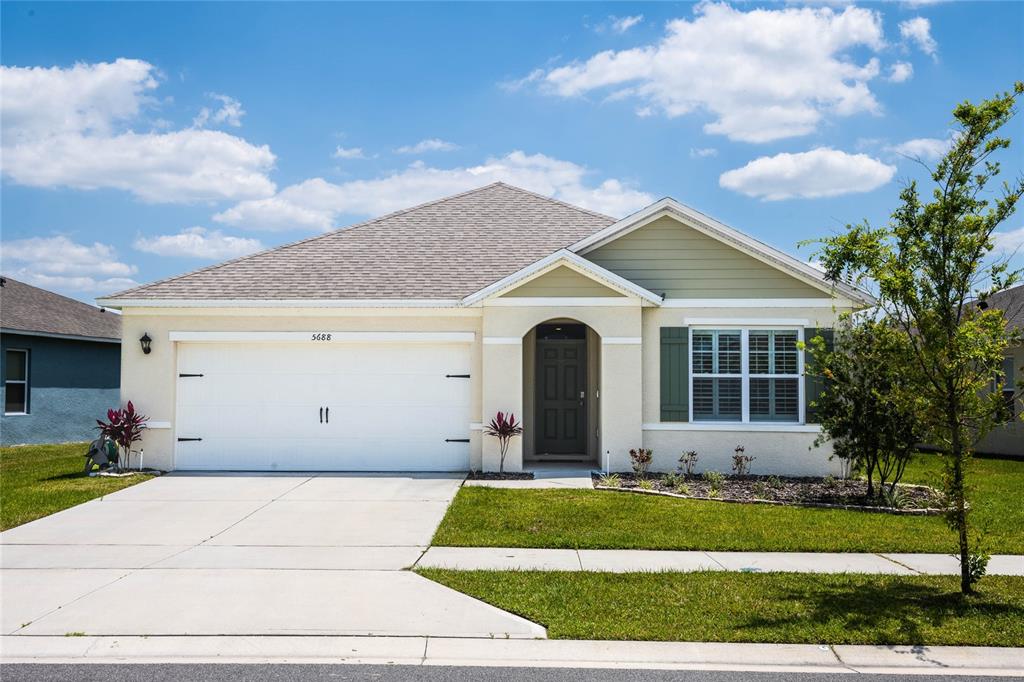 A single-story suburban house features a two-car garage, light stucco siding, and a front porch — 5688 SILTSTONE STREET, LAKELAND, FL