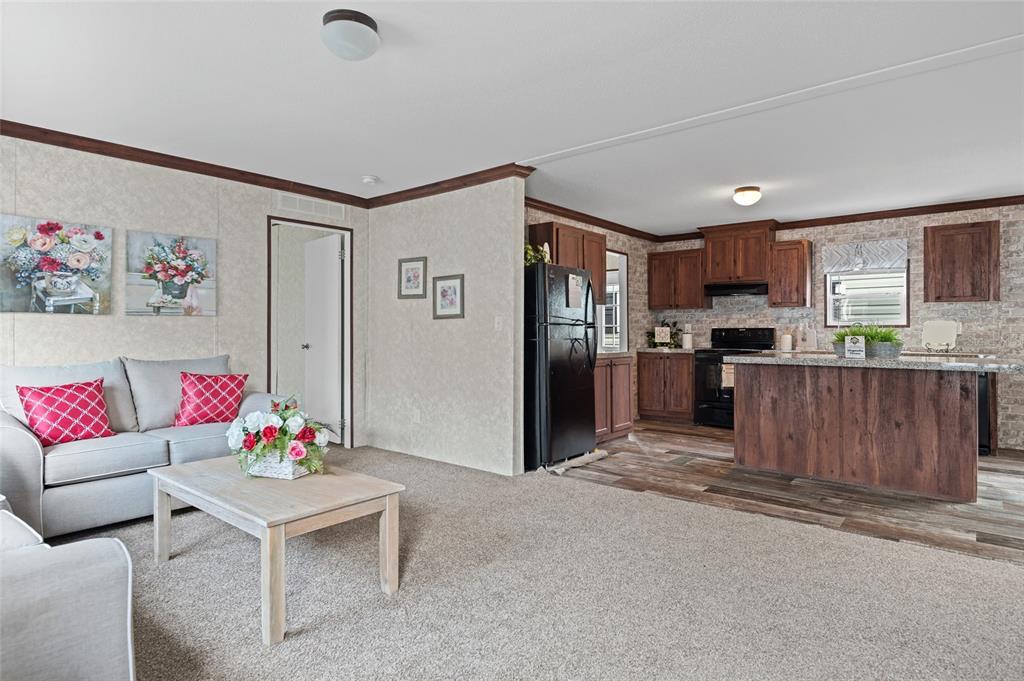 An open-concept living room with carpeted floors flows into a kitchen featuring dark wood cabinetry — 19836 NW 280TH STREET, OKEECHOBEE, FL