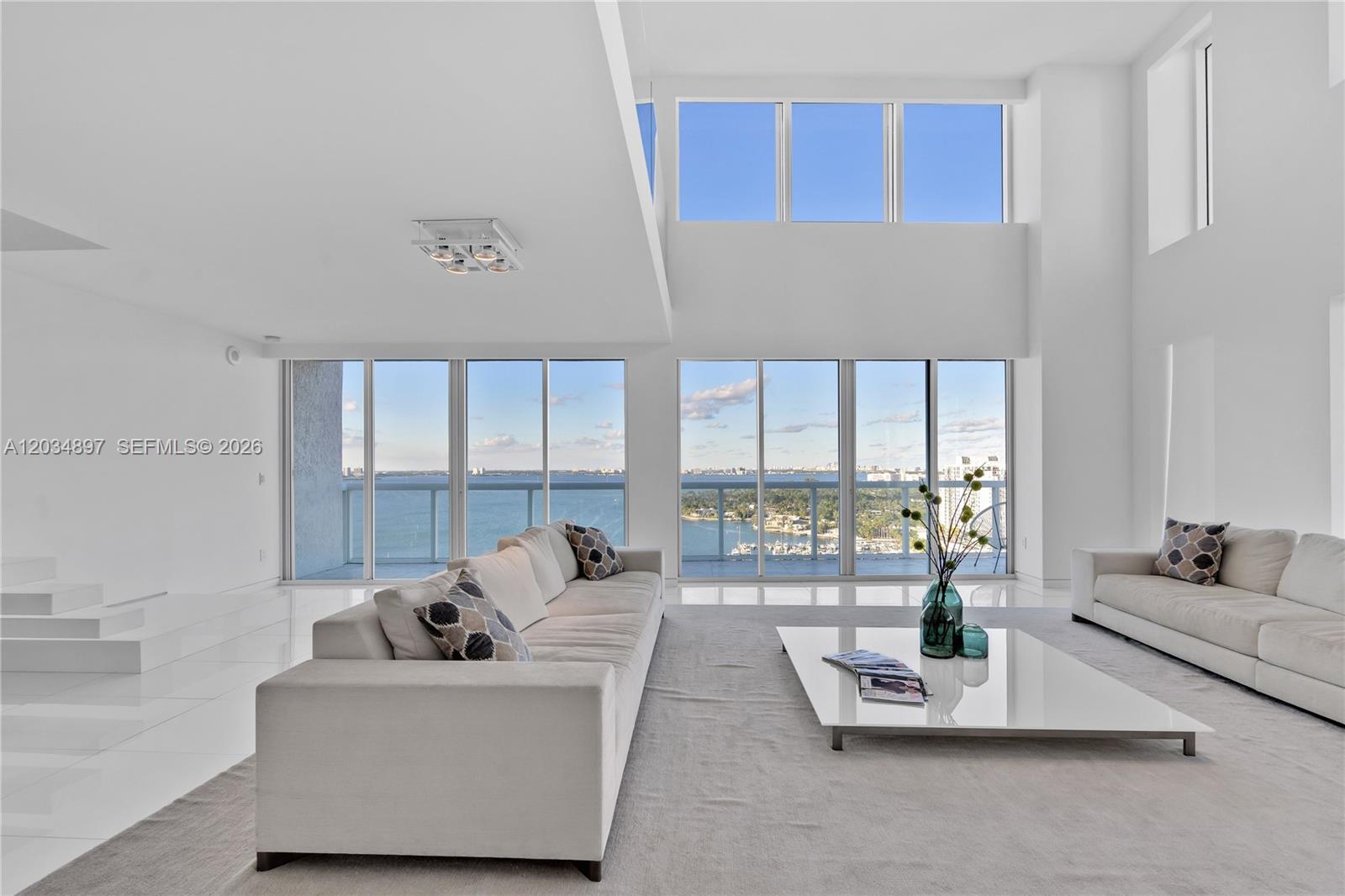 A bright, modern living room features white sofas, a low coffee table, and floor-to-ceiling windows — 10 Venetian Way, Miami Beach FL 33139, MIAMI BEACH, FL