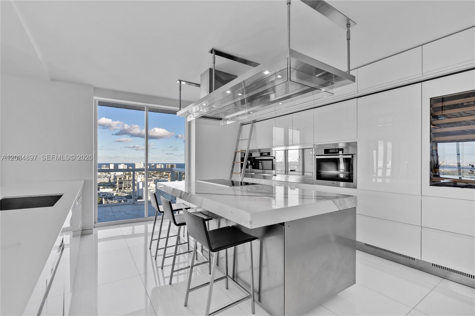 A modern white kitchen features a marble island, stainless steel appliances, and a balcony view — 10 Venetian Way, Miami Beach FL 33139, MIAMI BEACH, FL