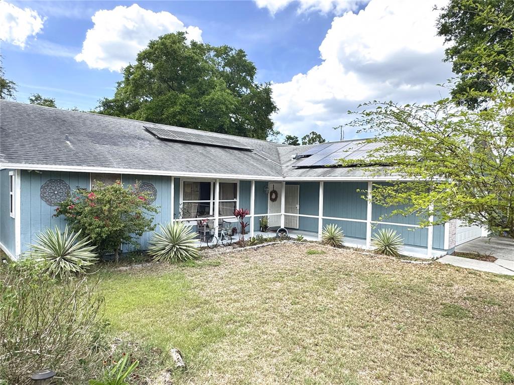 A single-story blue house with a covered porch, solar panels, and a front lawn — 2098 BRENT PLACE, PALM HARBOR, FL