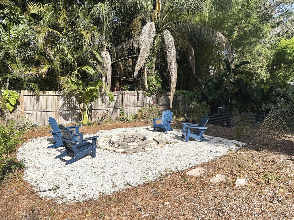 A backyard fire pit area features four blue Adirondack chairs on a white gravel patio — 2098 BRENT PLACE, PALM HARBOR, FL