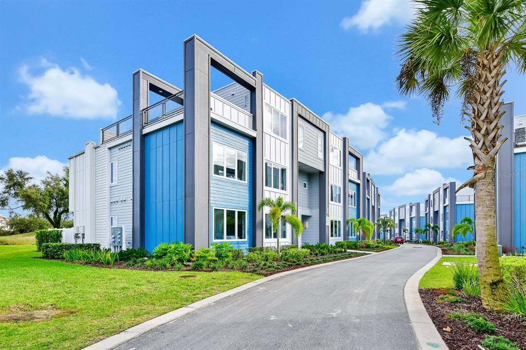A modern multi-story apartment building with blue and white siding stands beside a paved road — 7740 SANDY RIDGE DRIVE UNIT 113, REUNION, FL
