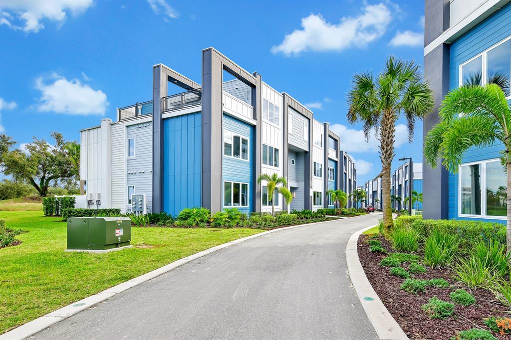 A paved driveway leads toward modern multi-story apartment buildings with blue and white siding — 7740 SANDY RIDGE DRIVE UNIT 113, REUNION, FL