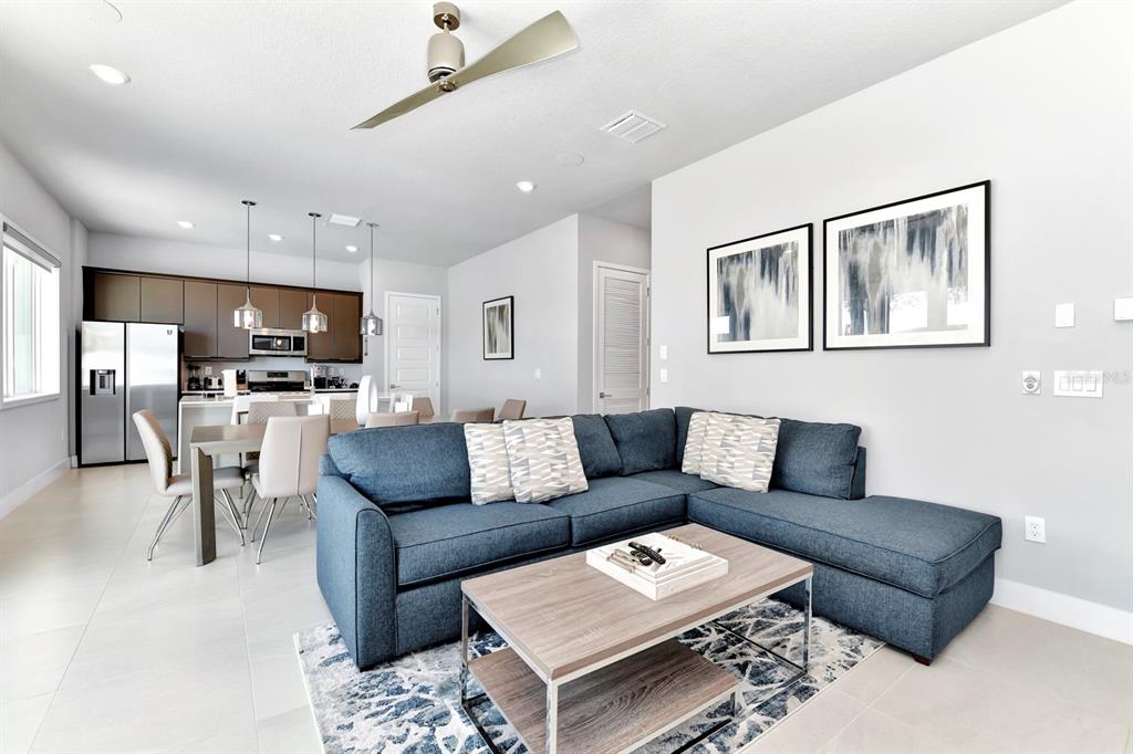 A modern living room with a blue sectional sofa, coffee table, and adjacent open kitchen — 7740 SANDY RIDGE DRIVE UNIT 113, REUNION, FL