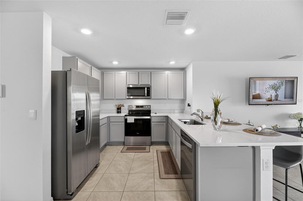 A modern kitchen features gray cabinets, stainless steel appliances, and a white quartz island countertop — 3345 BLUE ESTUARY ROAD, WIMAUMA, FL