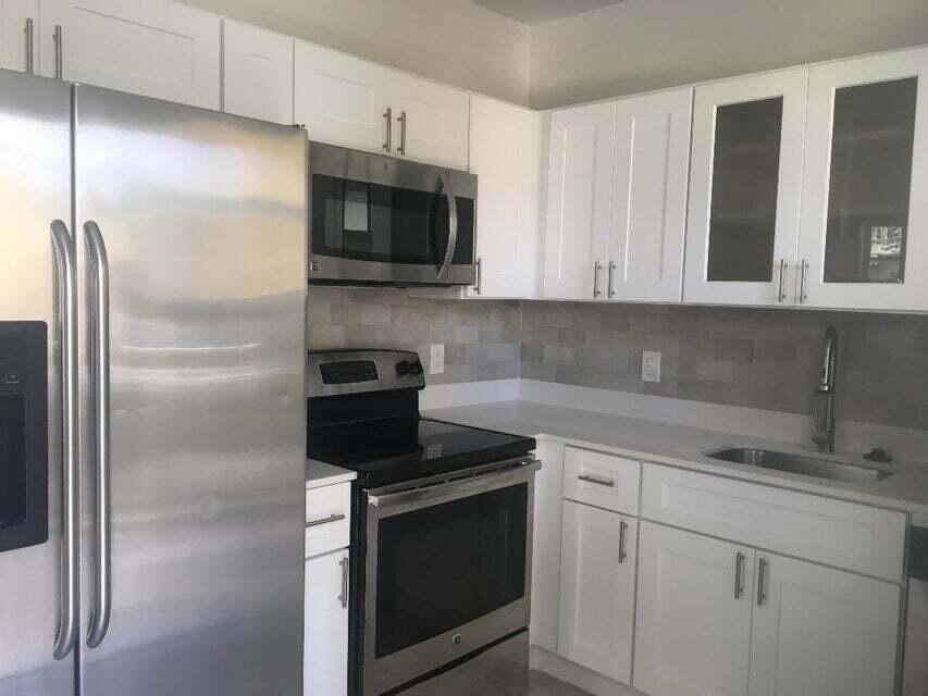 A kitchen features white cabinets, stainless steel appliances, a gray tile backsplash, and white countertops — 407 S Lakeside Drive # A, FL 33460, FL