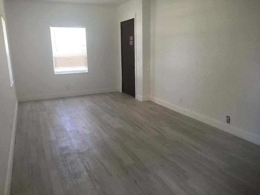 An empty room with light wood-look flooring, white walls, a window, and a dark door — 407 S Lakeside Drive # A, FL 33460, FL