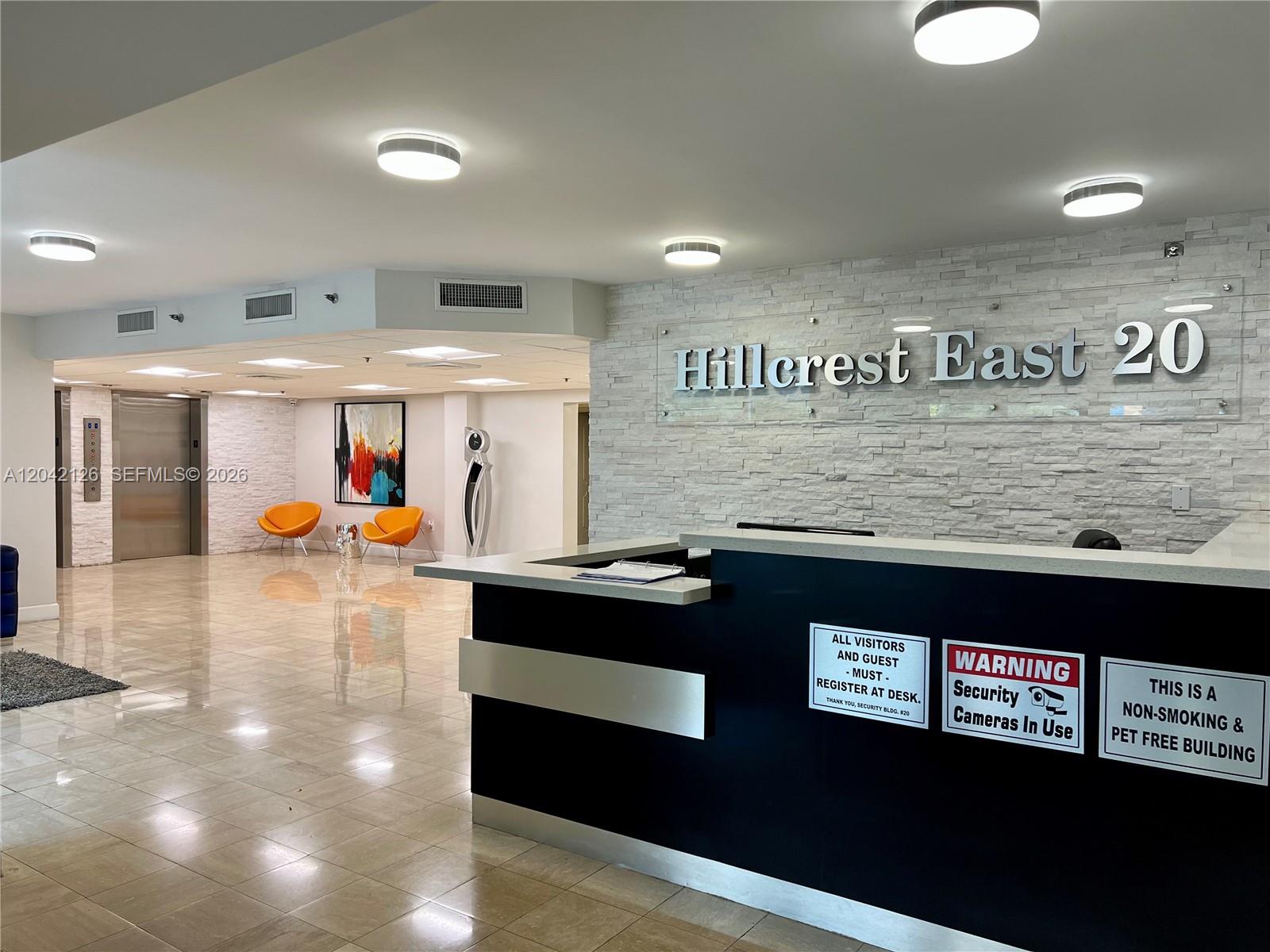 A modern building lobby features a reception desk, stone accent wall, and orange lounge chairs — 919 Hillcrest Dr # 102, Hollywood FL 33021, HOLLYWOOD, FL