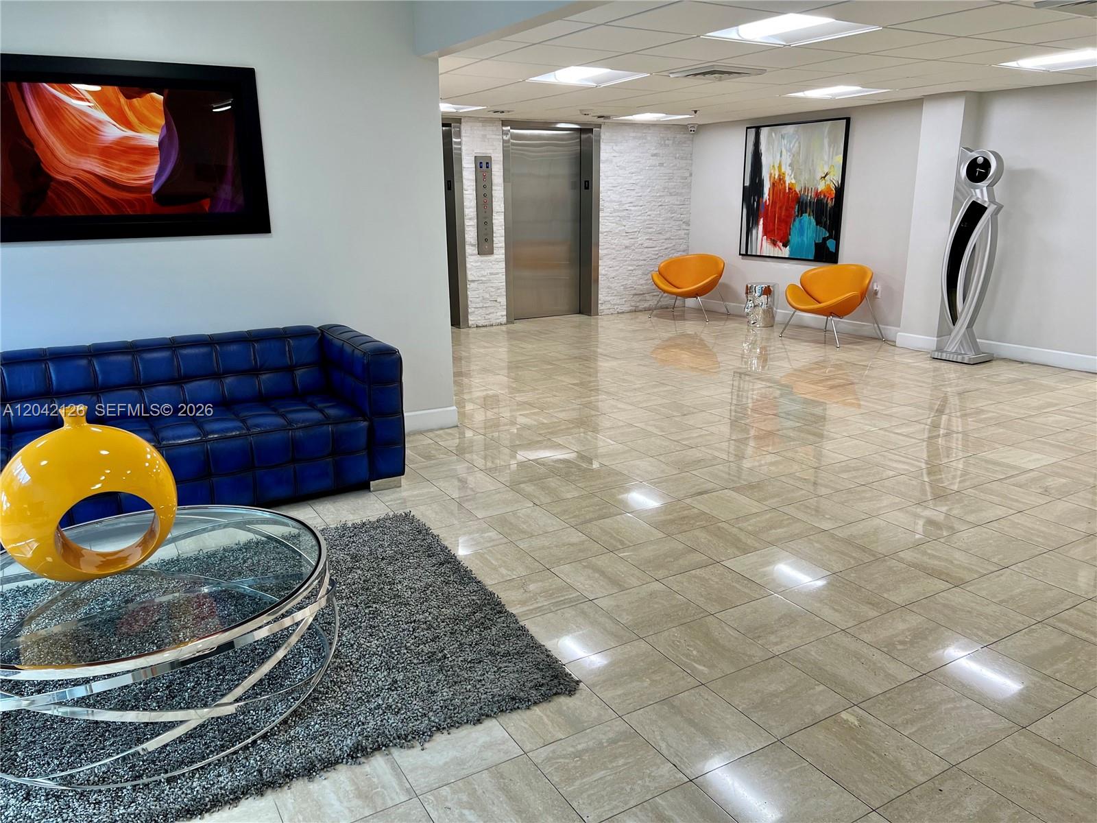A modern lobby features a blue tufted sofa, orange accent chairs, and polished tile floors — 919 Hillcrest Dr # 102, Hollywood FL 33021, HOLLYWOOD, FL