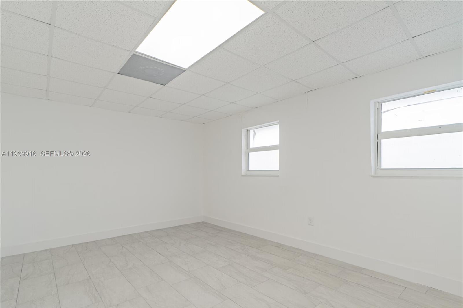 An empty room features white walls, light-colored tile flooring, and a drop ceiling — 1615 W 31st Pl, Hialeah FL 33012, HIALEAH, FL