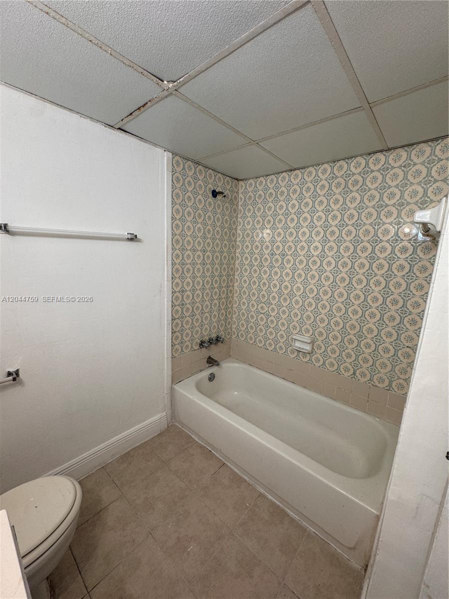 A bathroom features a white bathtub, patterned tile walls, and a drop ceiling — 1756 NW 55th Ave # 101, Lauderhill FL 33313, LAUDERHILL, FL