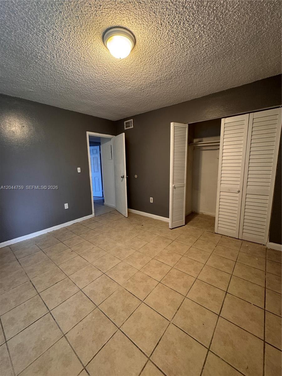 A bedroom with dark gray walls, beige tile flooring, and white louvered closet doors — 1756 NW 55th Ave # 101, Lauderhill FL 33313, LAUDERHILL, FL
