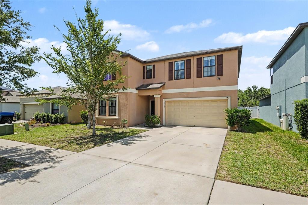 A two-story tan stucco house with a two-car garage and a concrete driveway — 10022 CARLOWAY HILLS DRIVE, WIMAUMA, FL