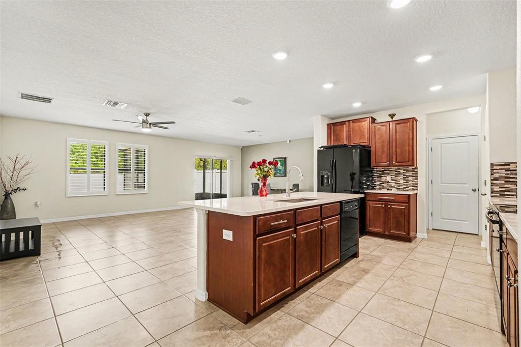 A kitchen with dark wood cabinets, a central island, and tile flooring opens to a living area — 10022 CARLOWAY HILLS DRIVE, WIMAUMA, FL
