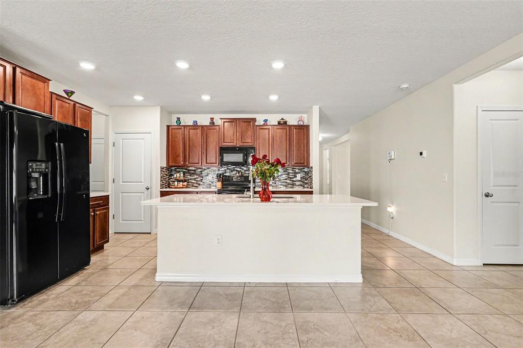 A kitchen features a central island, dark wood cabinets, a black refrigerator, and tile flooring — 10022 CARLOWAY HILLS DRIVE, WIMAUMA, FL