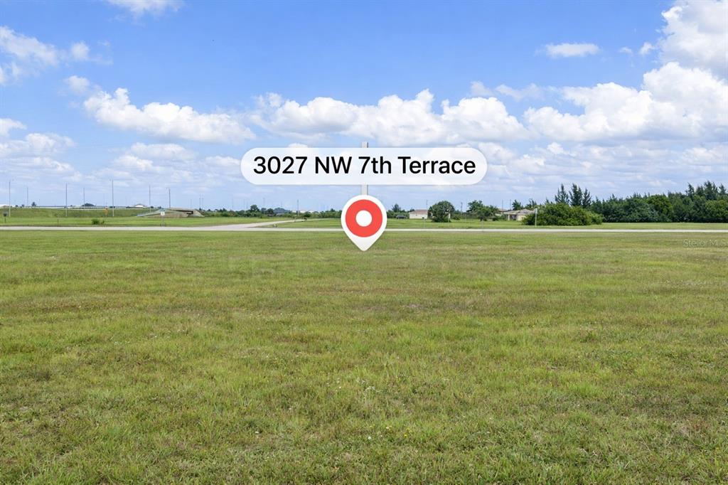 A wide, grassy vacant lot is shown under a blue sky with scattered clouds — 3027 NORTHWEST 7TH TERRACE, CAPE CORAL, FL
